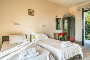 A room with two beds, a wardrobe, a small table, and a door leading to an outdoor area.