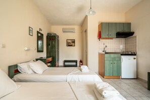 A room with two beds, a kitchenette, a mirror, an air conditioner, and a framed picture on the wall.