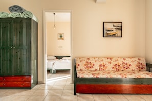 A room with a green wardrobe, a floral sofa, a bed, and a painting on the wall.