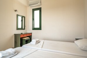 Une chambre d’hôtel avec deux lits, un petit bureau avec un miroir, une fenêtre et un climatiseur fixé au mur.