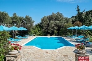 Una piscina con sombrillas azules, sillas de descanso y un patio de piedra.