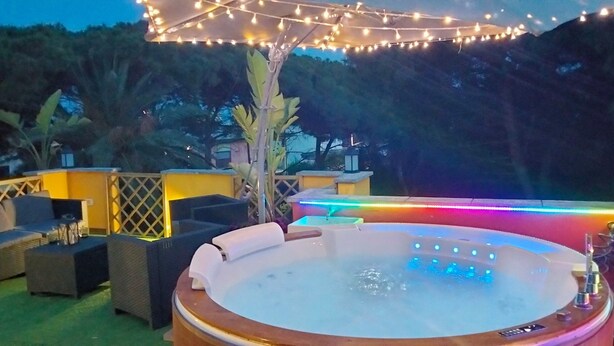 A hot tub with a wooden edge, surrounded by outdoor seating and string lights. - Holiday Home 'Apt in Serra' with Private Pool, Wi-Fi & Air Conditioning (Quartu Sant'Elena)