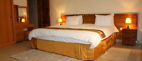 A hotel room with a large bed, wooden headboard, two bedside tables with lamps, a wooden wardrobe, and a mirror.
