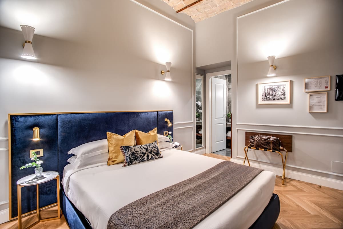 A modern bedroom with a large bed, bedside lamps, a small table with a vase, and a coat rack.