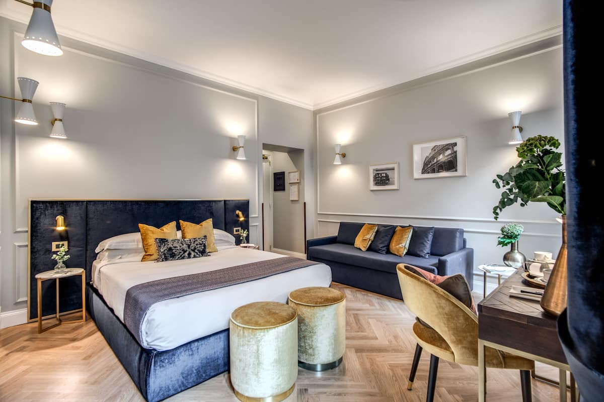 A modern hotel room with a large bed, a sofa, a desk, and a potted plant.