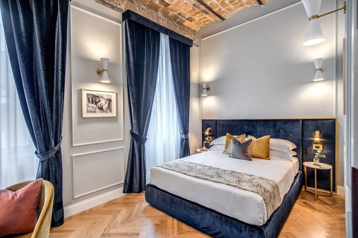 A modern bedroom with a large bed, dark curtains, and wall-mounted lights.