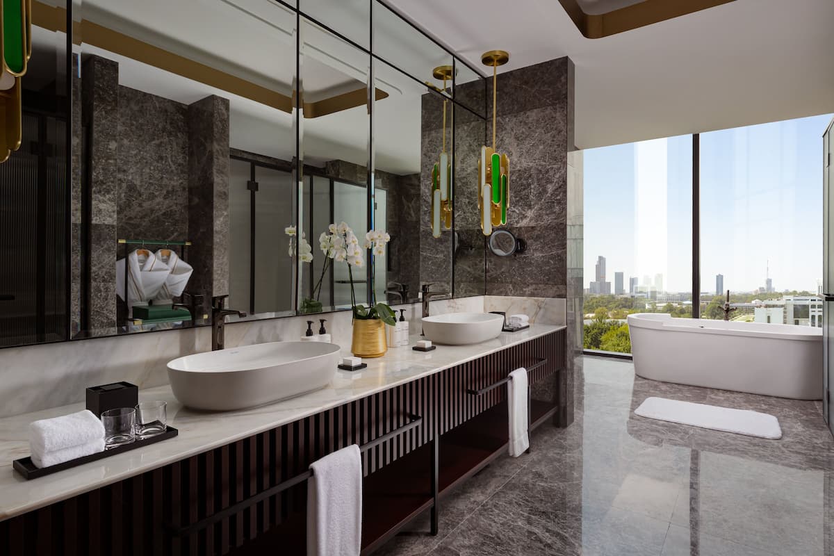 A modern bathroom with a large mirror, two sinks, a bathtub, and a view of the city.