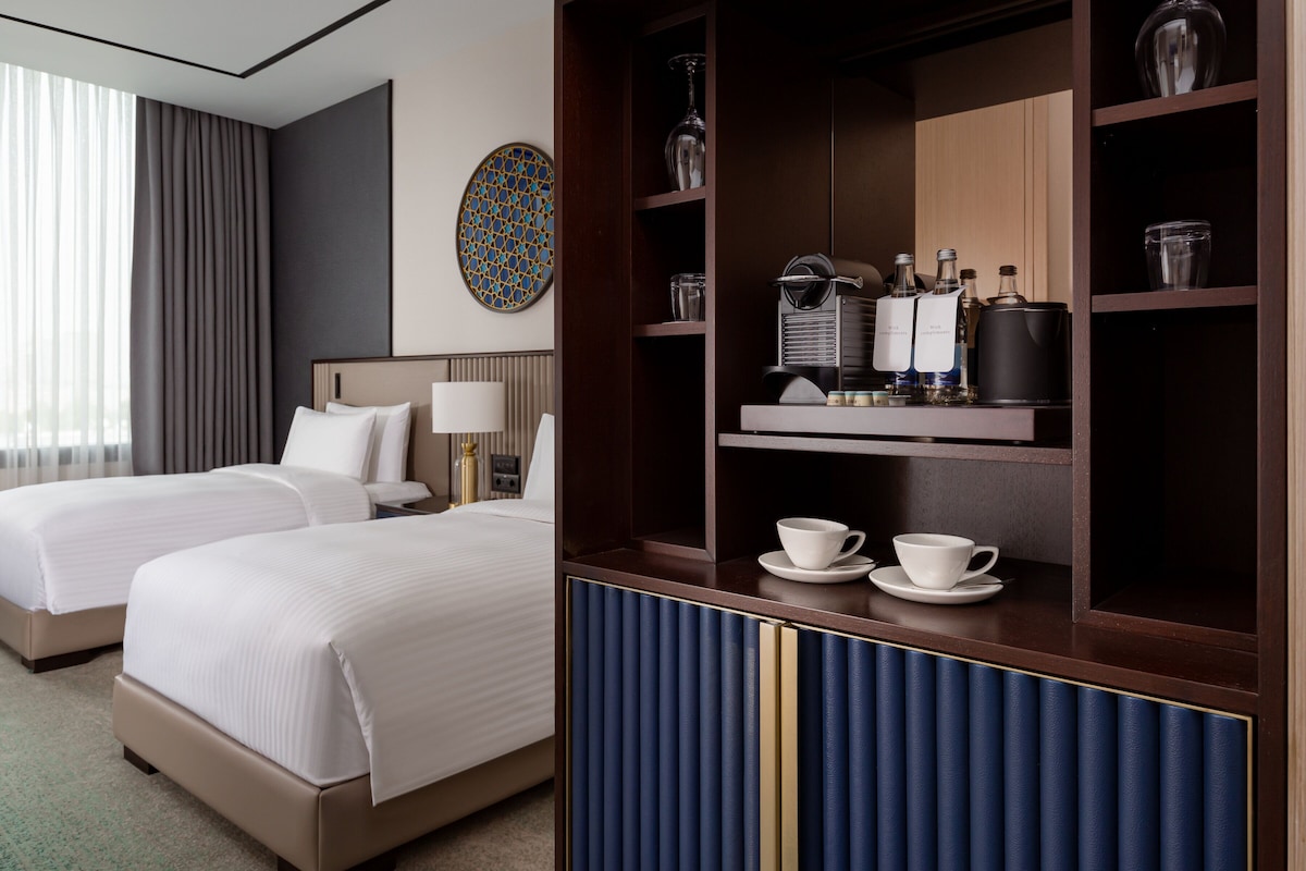 A hotel room with two beds, a coffee station, and a decorative wall piece.