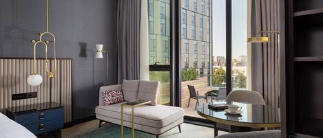 Une chambre d’hôtel moderne dotée d’une grande fenêtre, d’un canapé, d’une petite table et d’un bureau avec une lampe.