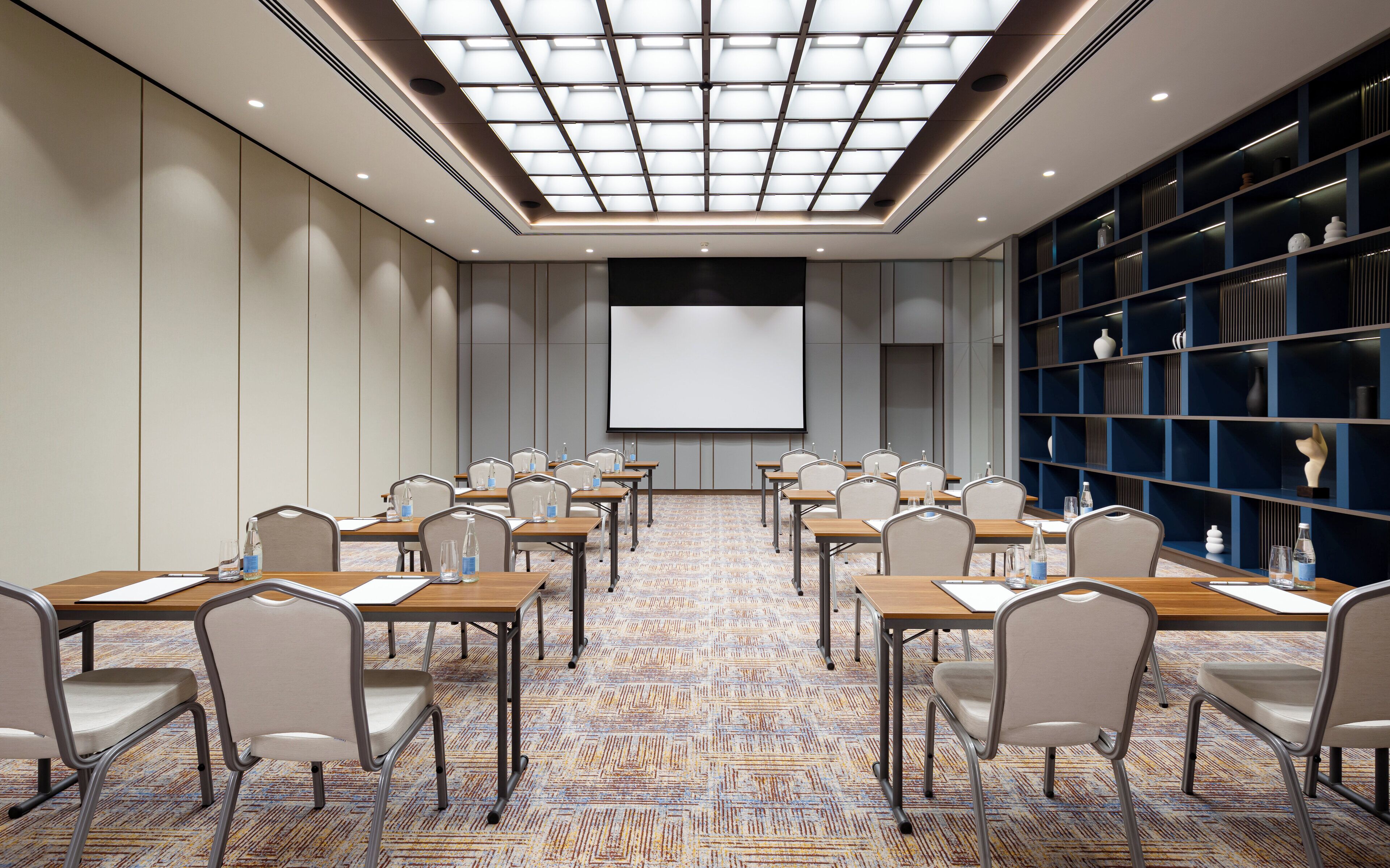 A conference room with a large screen, tables, chairs, and a patterned carpet.