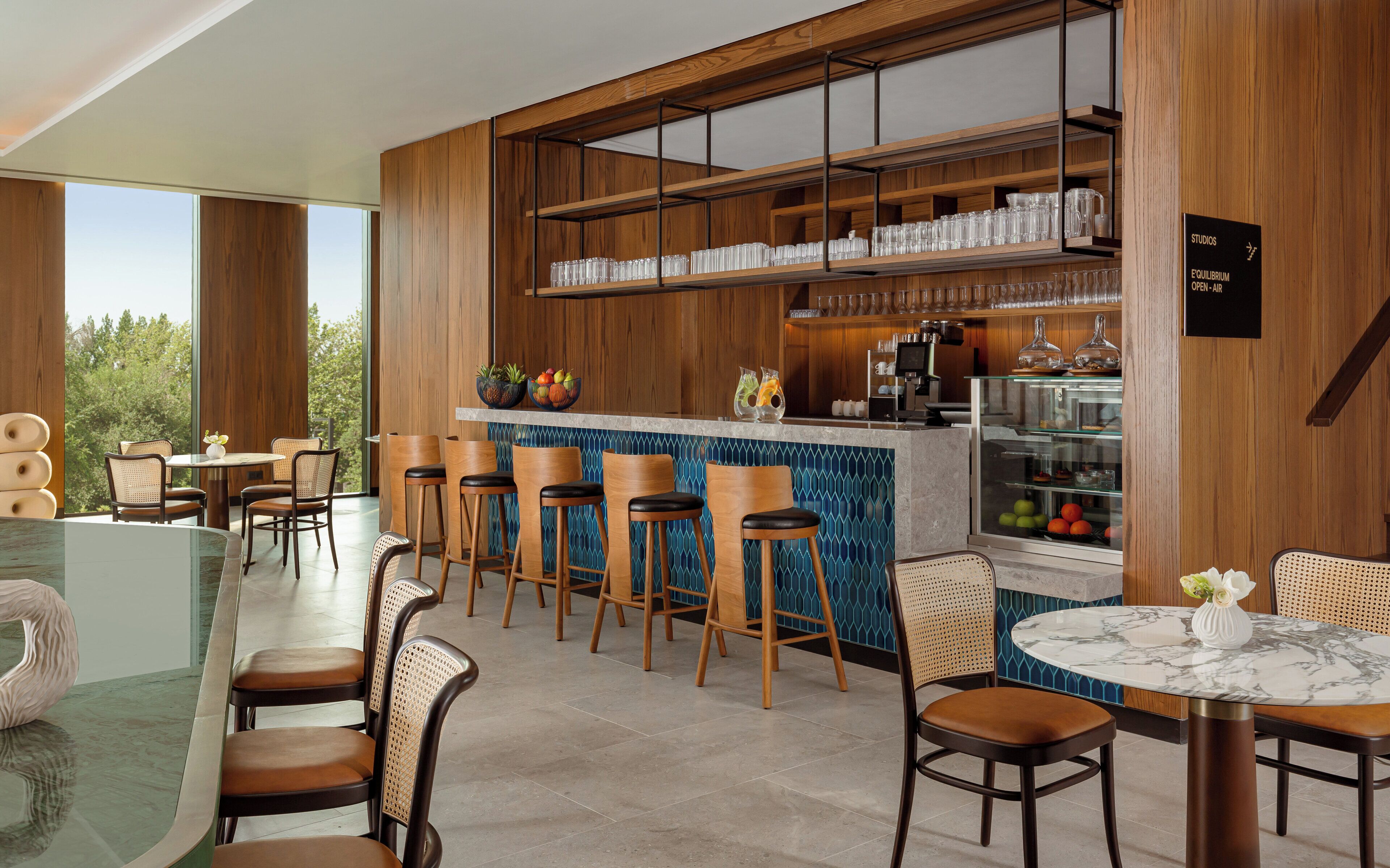 A modern bar area with wooden shelves, bar stools, and a marble-topped table.
