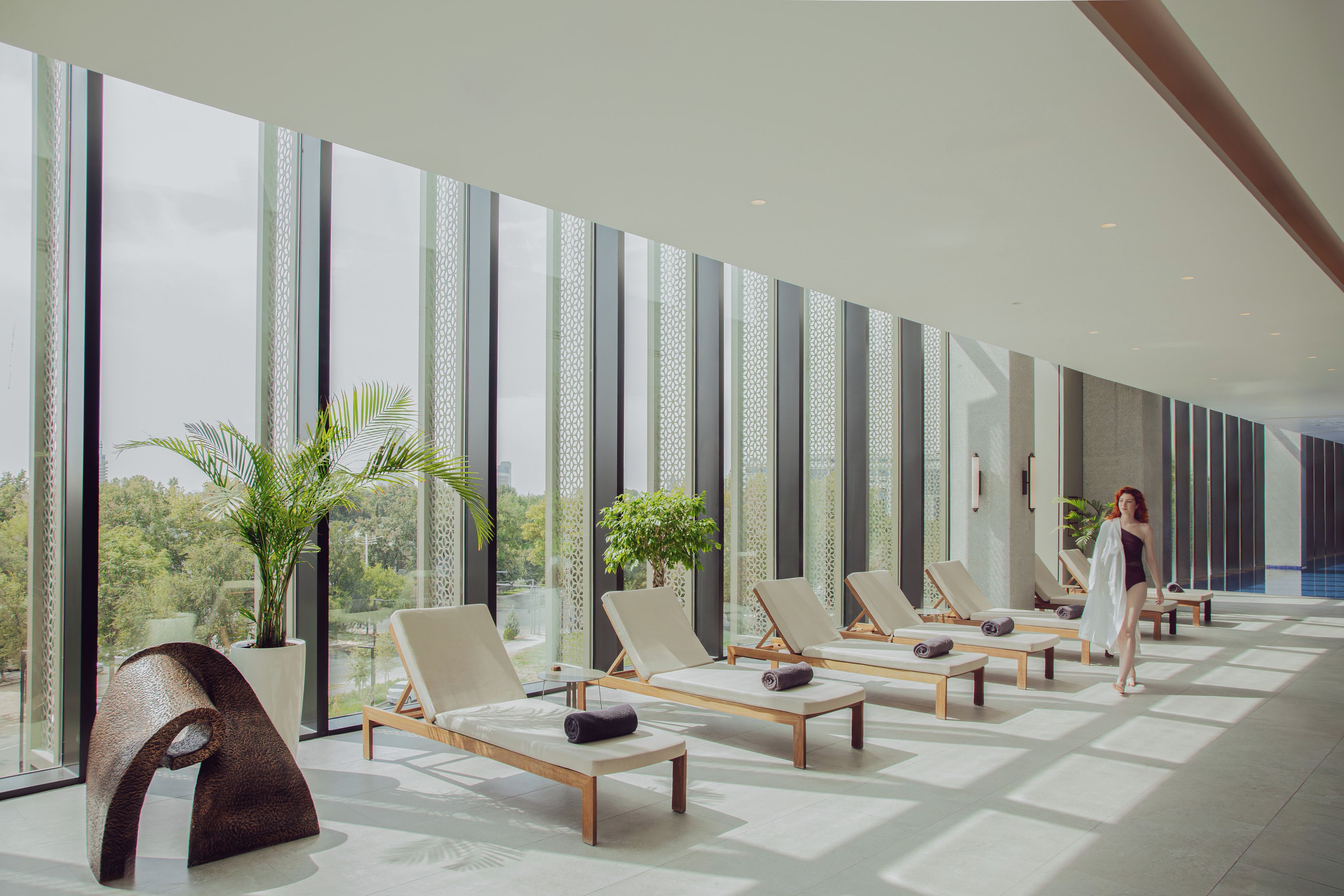A modern spa area with sun loungers, large windows, and indoor plants.