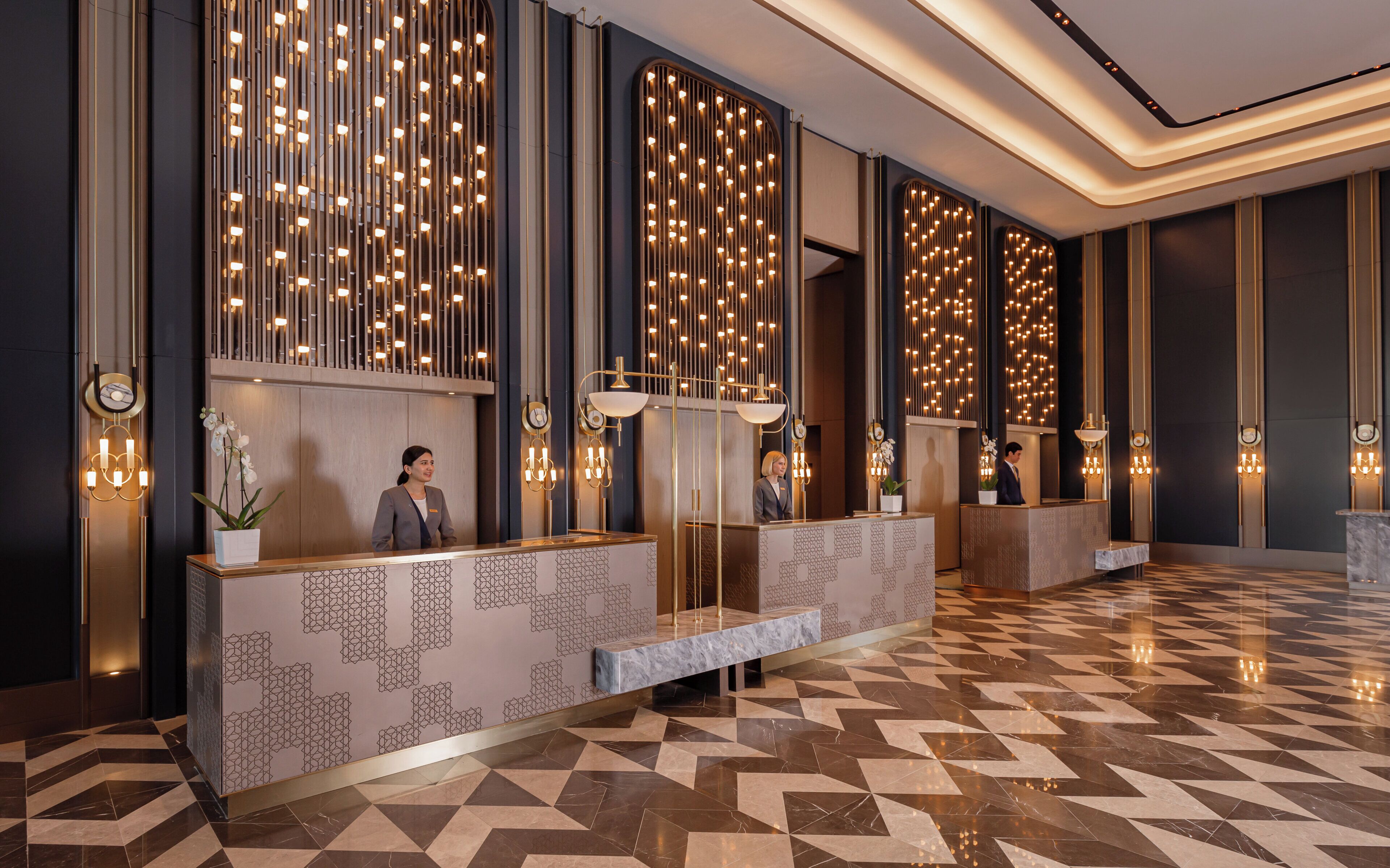 Zona de recepción de un hotel con diseño moderno, que presenta un suelo estampado, un mostrador de recepción e iluminación decorativa en la pared.