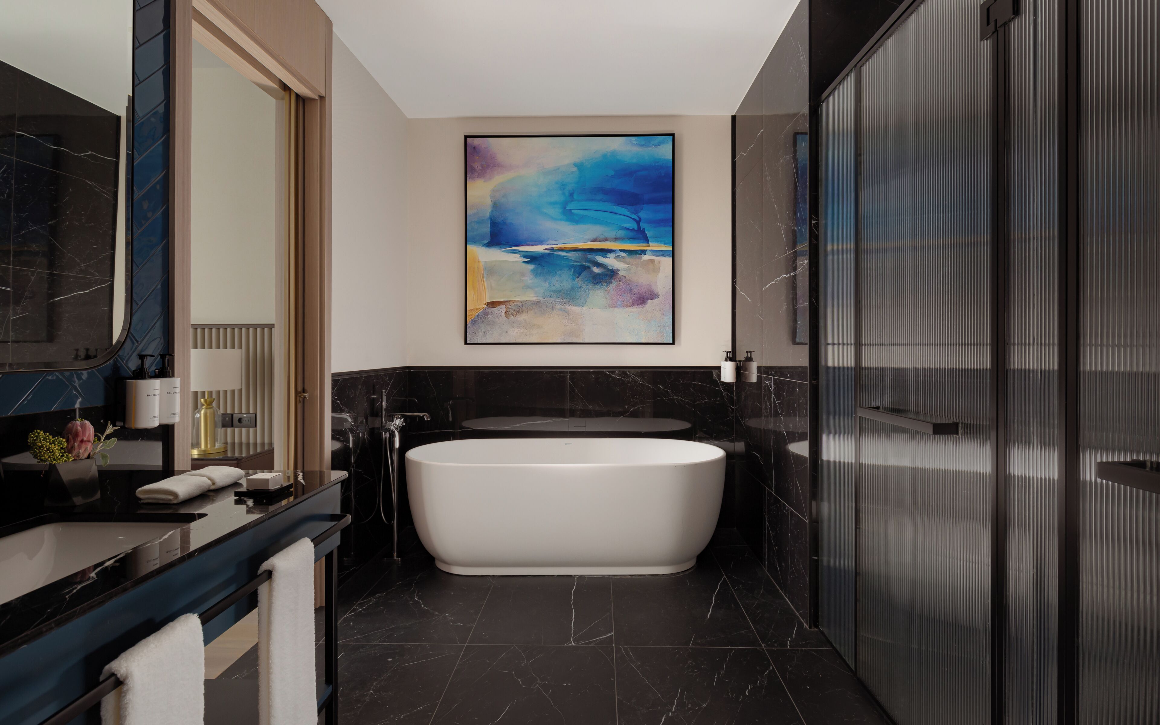 A modern bathroom with a freestanding bathtub, a large mirror, and a contemporary abstract painting.