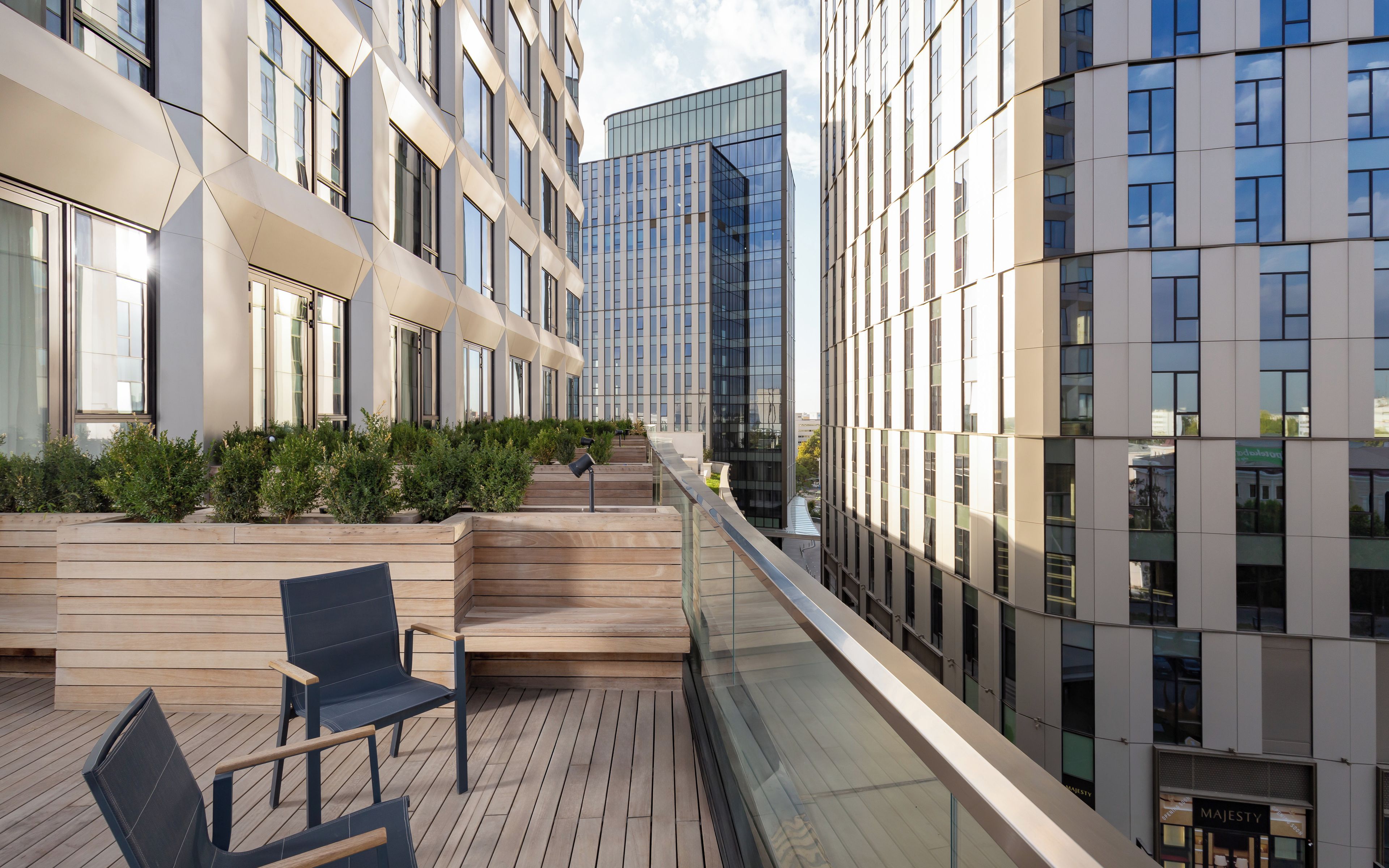 A modern building with a glass facade, wooden deck with seating, and a clear sky.