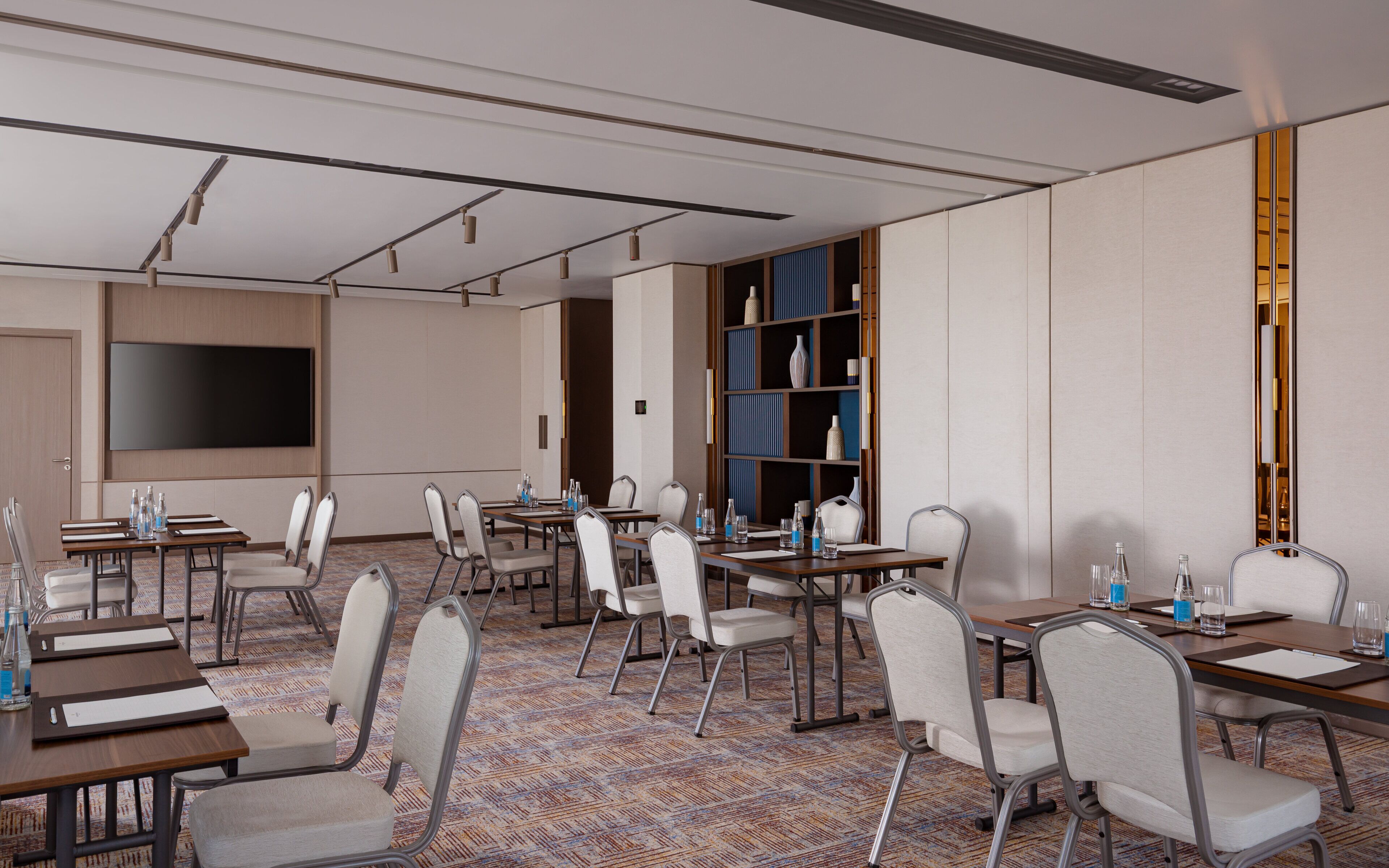A conference room with tables, chairs, a large flat-screen TV, and a bookshelf.