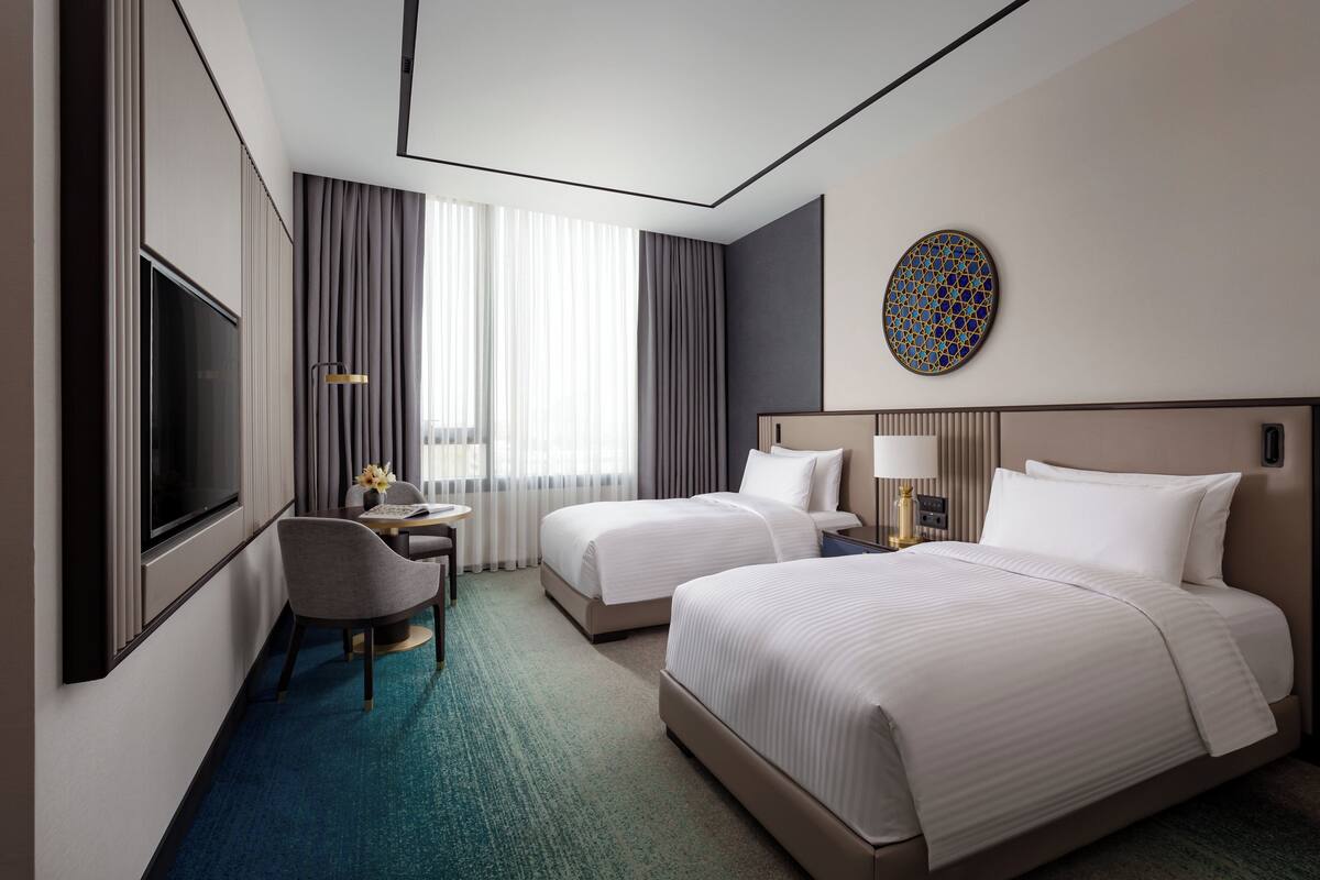 A hotel room with two beds, a desk with a chair, a TV, and a decorative wall piece.