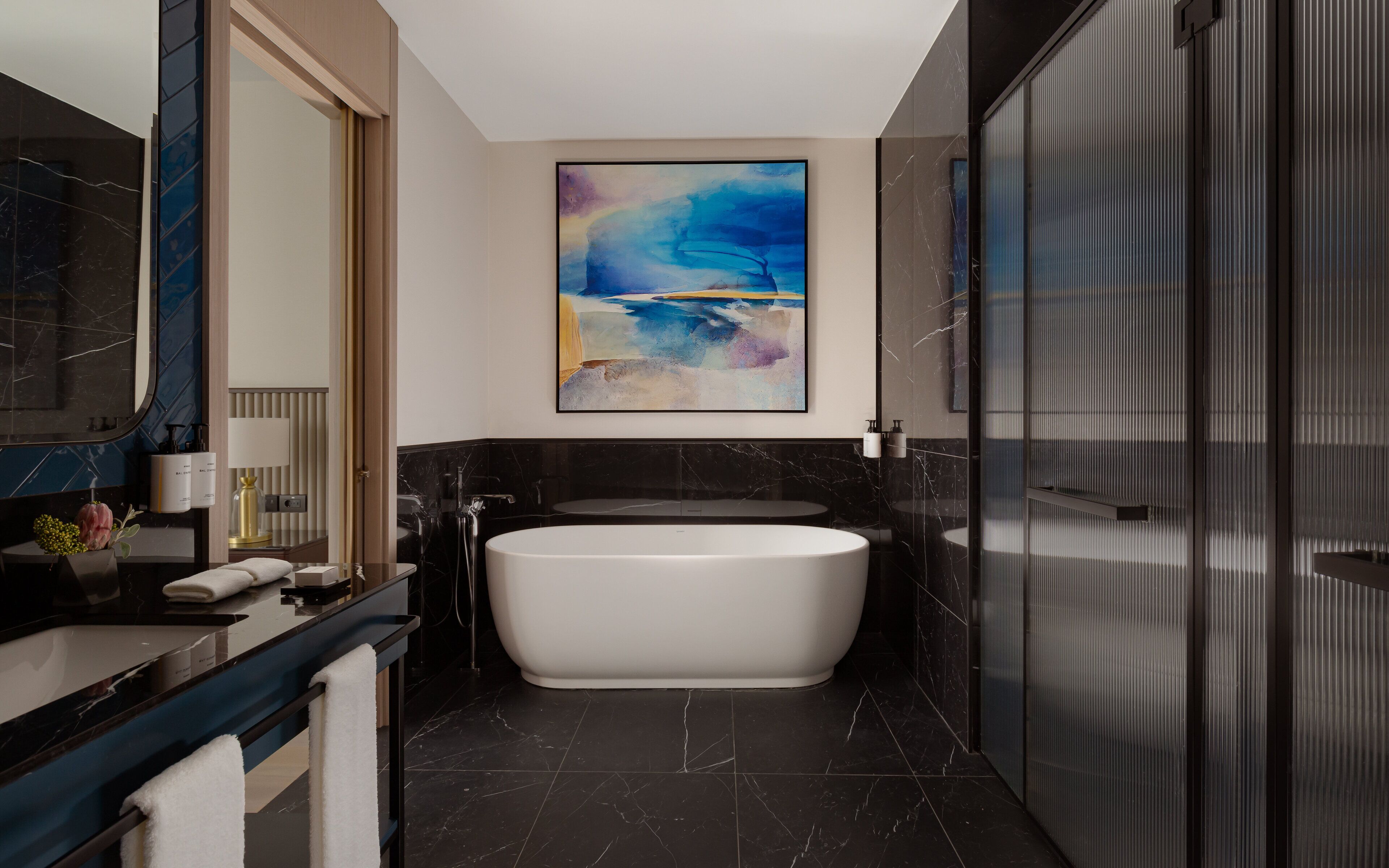 Un baño moderno con una bañera independiente, un espejo grande y un cuadro abstracto contemporáneo.