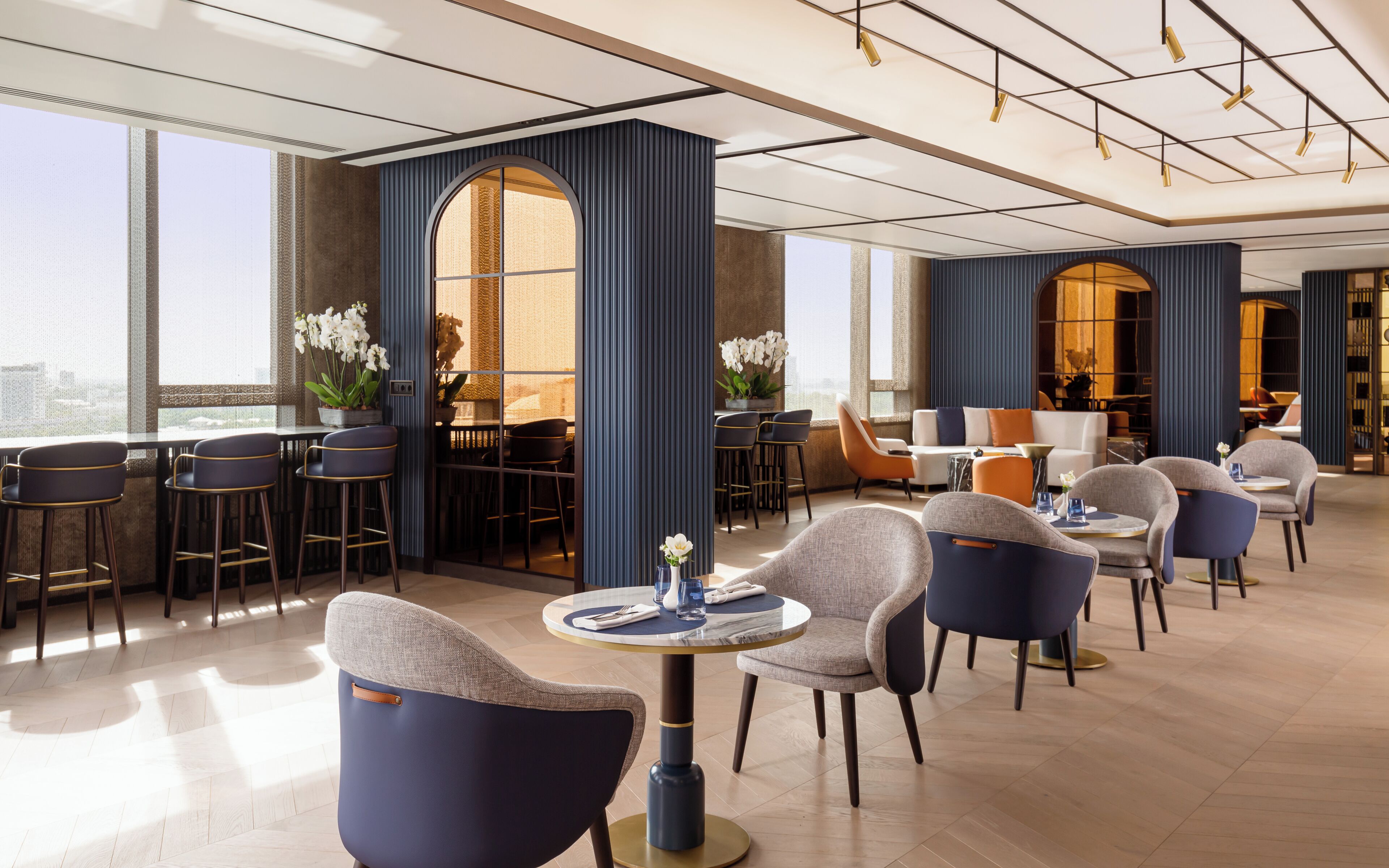 Een moderne hotellobby met diverse zithoeken, waaronder barstoelen en fauteuils, en een eetgedeelte met een hoge tafel en stoelen.
