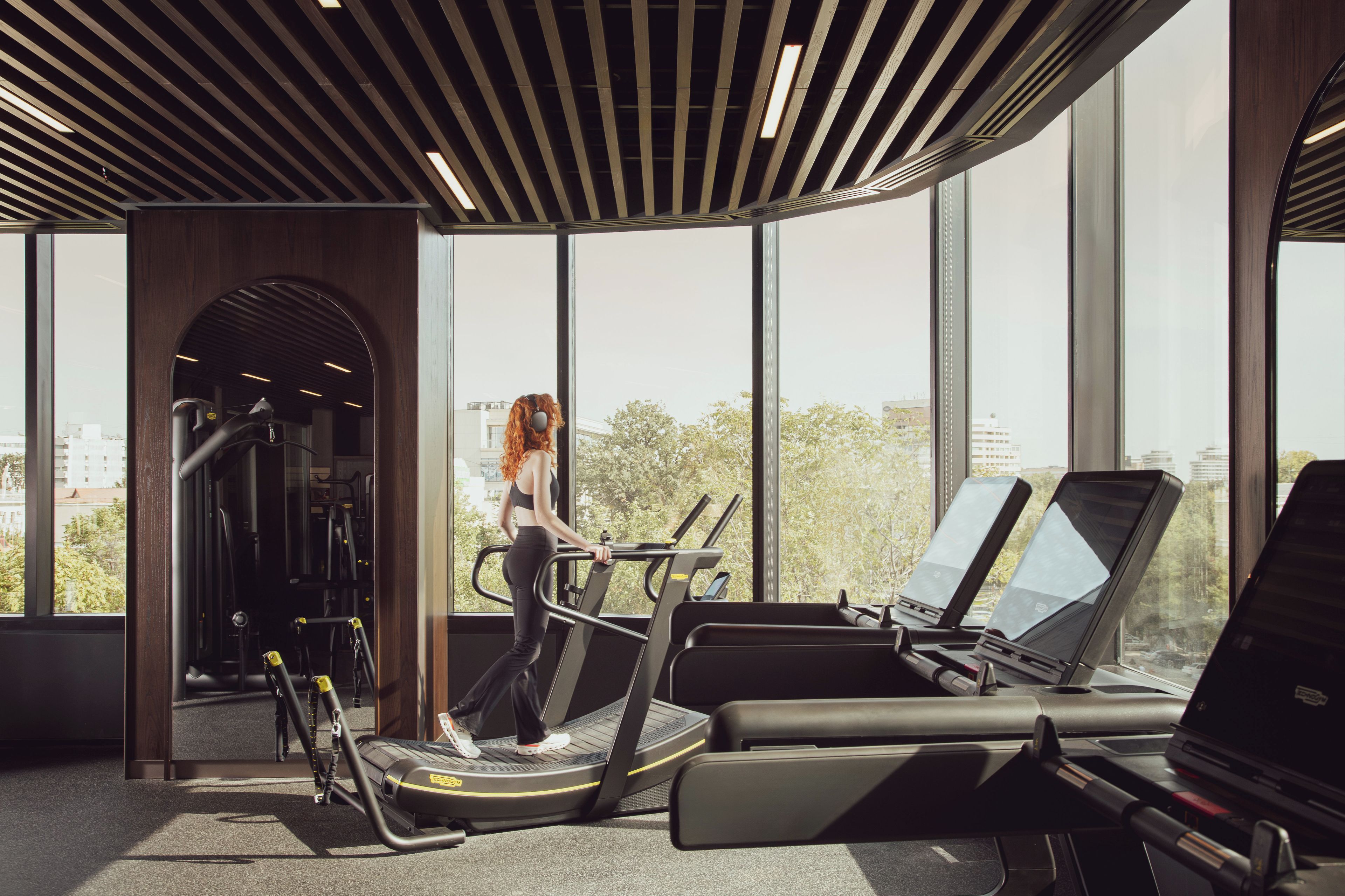 A gym with treadmills, exercise equipment, and large windows offering a view of the city.