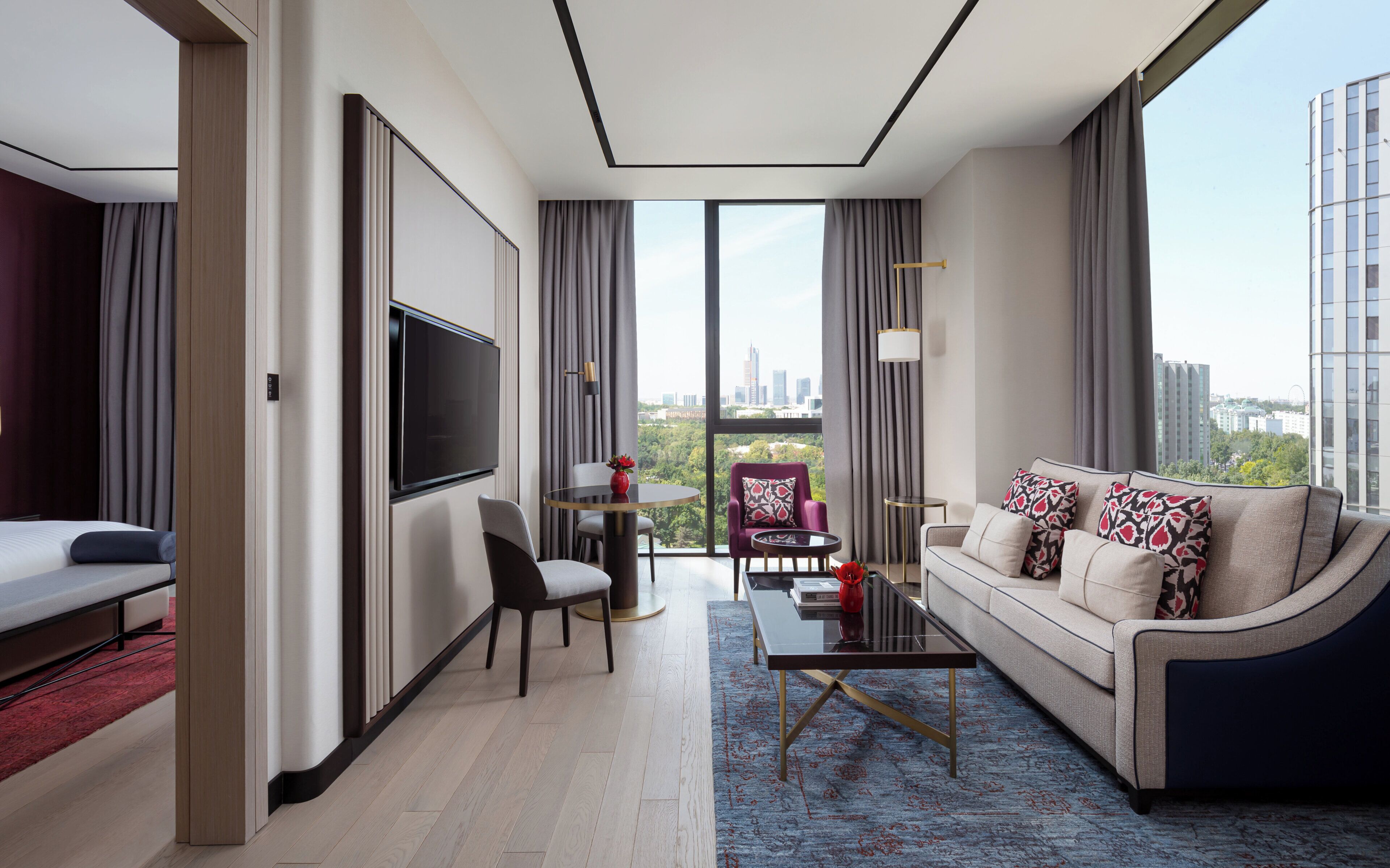 Une chambre d’hôtel moderne dotée d’une grande télévision, d’un canapé, d’un coin repas et offrant une vue sur le paysage urbain.