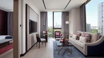 Une chambre d’hôtel moderne dotée d’une grande télévision, d’un canapé, d’un coin repas et offrant une vue sur le paysage urbain.