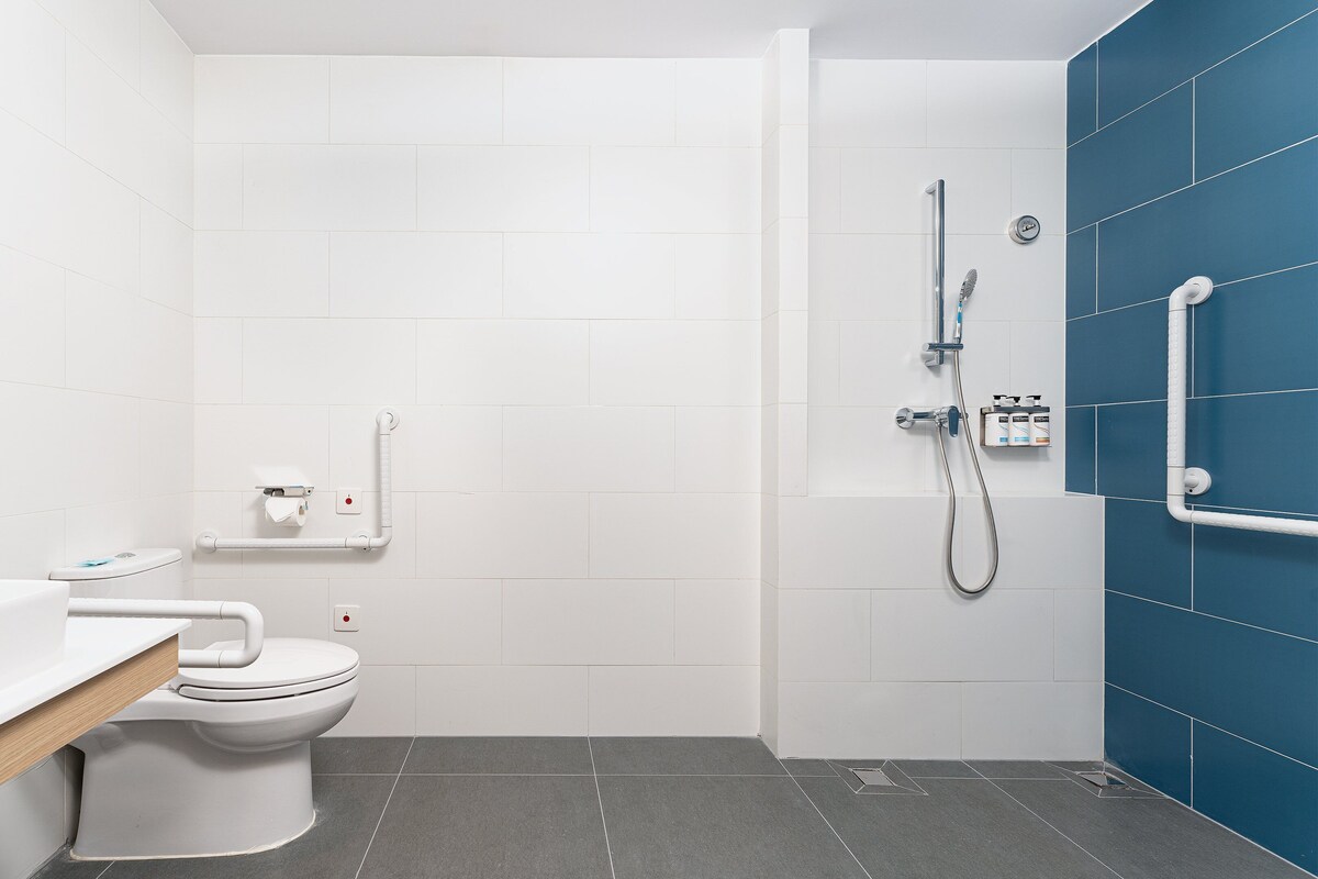 Un baño moderno con inodoro blanco, ducha con cabezal de ducha manual y pared de acento azul.