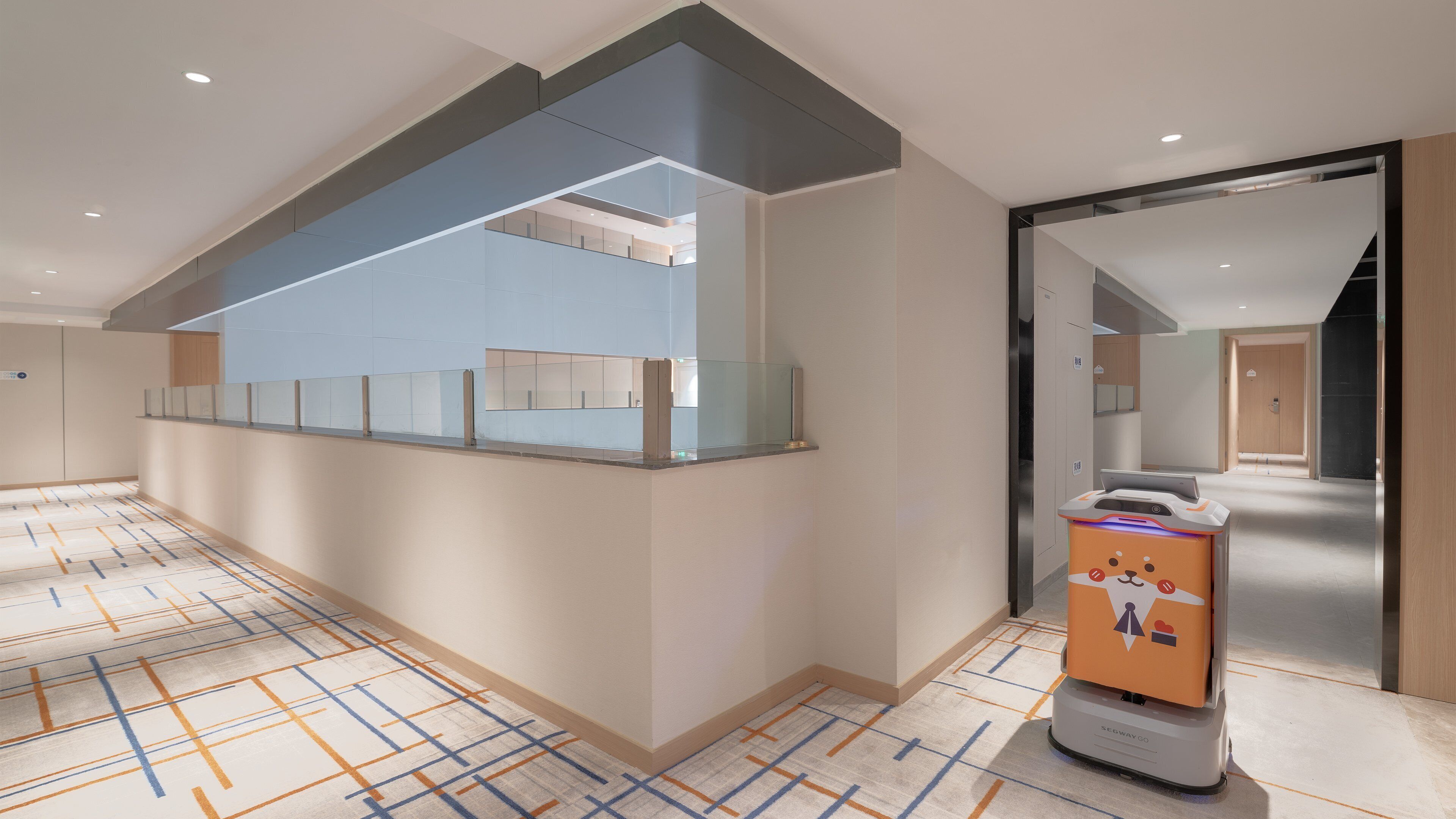 A modern hotel lobby with a glass partition, a vending machine, and a patterned carpet.