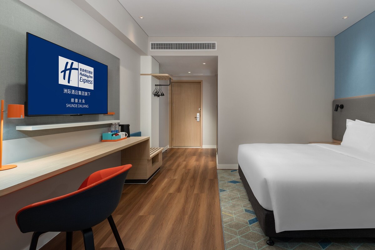 Una habitación de hotel con una cama, un escritorio con una silla, un televisor y una puerta que da a otra habitación.