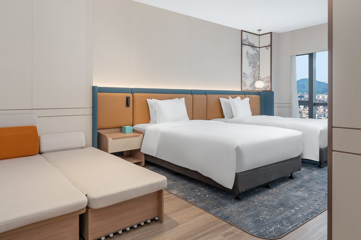 Habitación de hotel con una cama grande, un sofá, una mesita de noche y vistas a la ciudad.