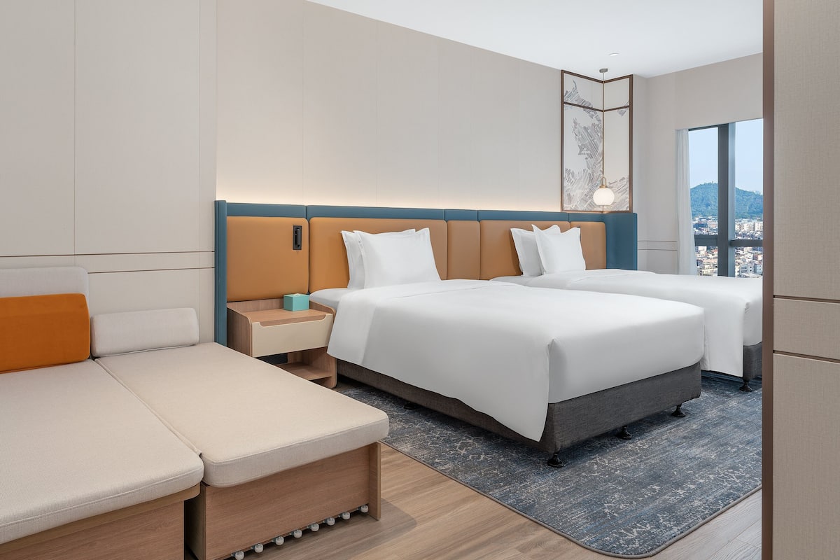 Ett hotellrum med en stor säng, en soffa, ett nattduksbord och utsikt över stadsbilden.