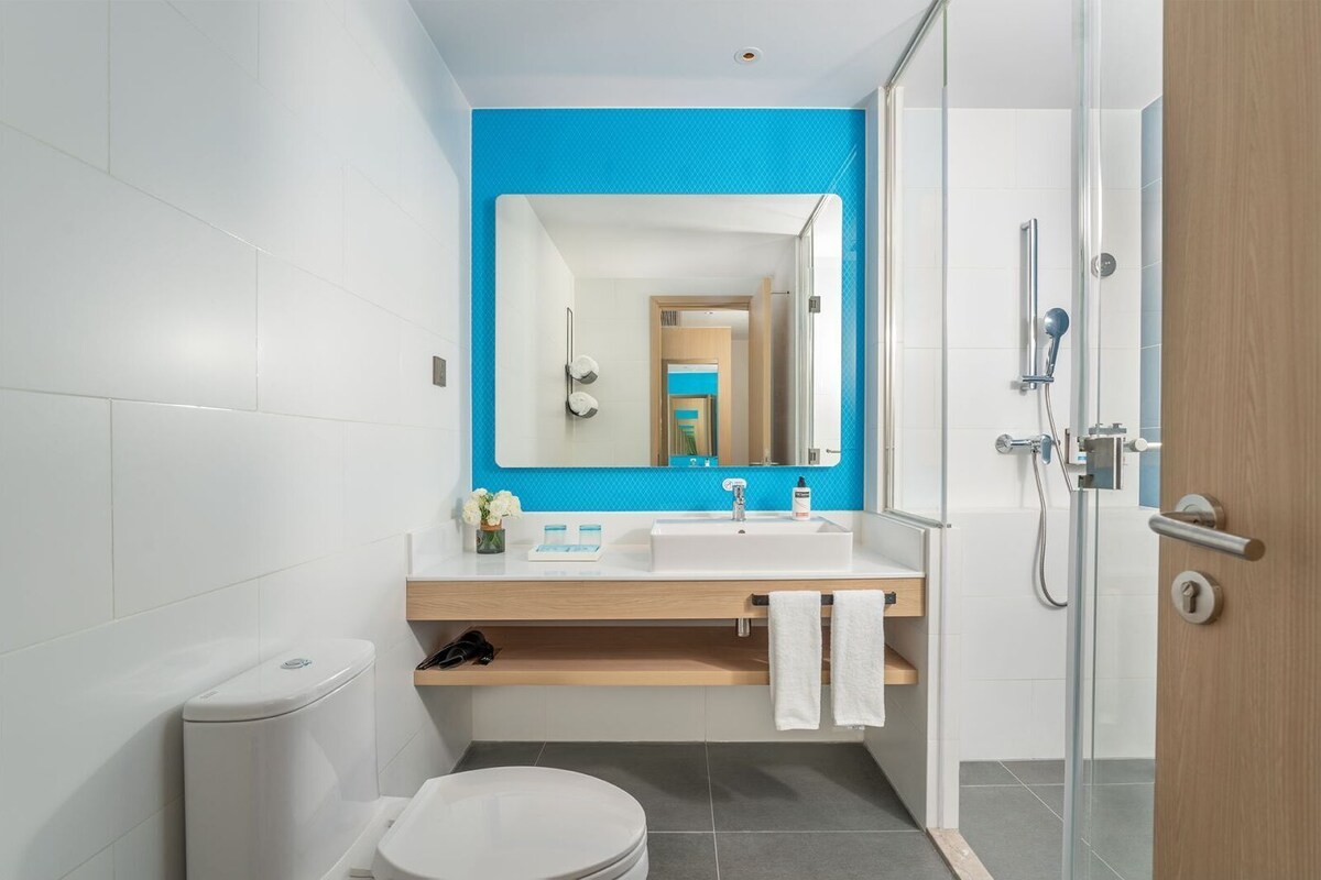 Un baño moderno con inodoro blanco, lavabo con espejo y zona de ducha.