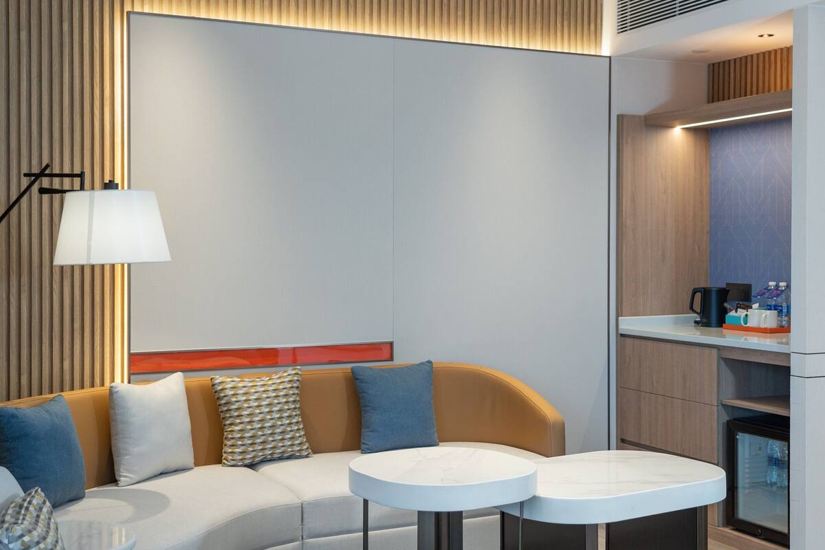 Ett modernt hotellrum med en soffa, två runda bord, en lampa och en liten köksdel.