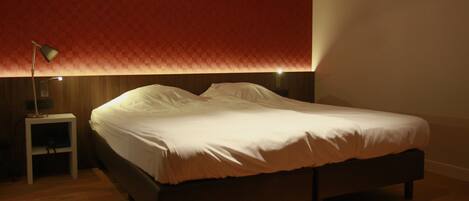 Una cama bien tendida en una habitación con suelo de madera y pared con estampado rojo.