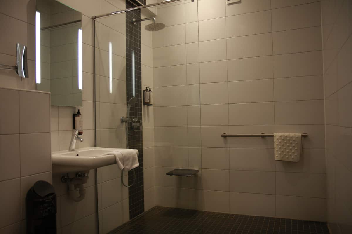 A modern bathroom with a sink, mirror, shower, and towel rack.