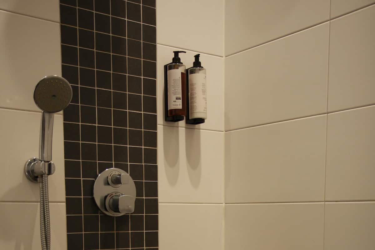 A shower area with a handheld showerhead, a wall-mounted control, and a shelf with toiletries.