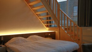 A bedroom with a large bed, a wooden staircase, and a window with curtains. - Hotel de Boskar Pelt (Pelt)