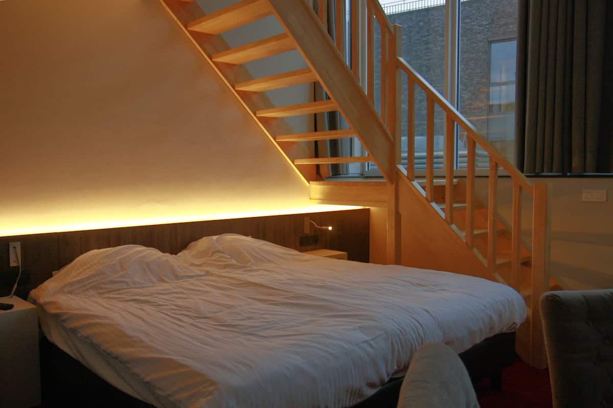 A bedroom with a large bed, a wooden staircase, and a window with curtains.