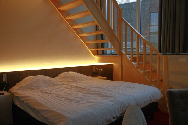 A bedroom with a large bed, a wooden staircase, and a window with curtains.