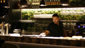 A bar area with shelves of bottles and glasses, a counter with a person working, and hanging lights. - Hotel de Boskar Pelt (Pelt)