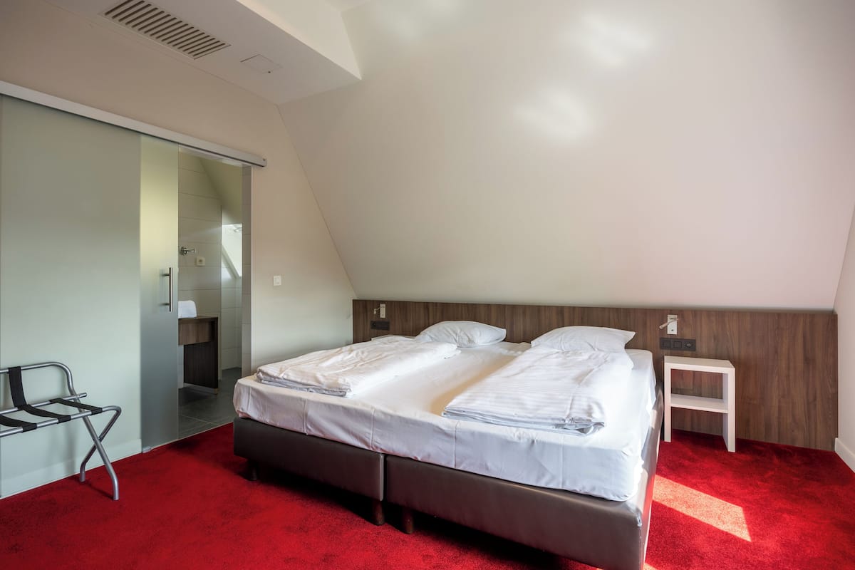 A modern hotel room with a large bed, a small bedside table, a chair, and a sliding door leading to a bathroom.