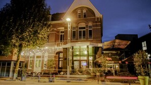 A hotel with a brick facade, large windows, outdoor seating, and string lights. - Hotel de Boskar Pelt (Pelt)