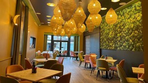 A restaurant interior with multiple tables and chairs, warm lighting, and a green leafy wall. - Hotel de Boskar Pelt (Pelt)