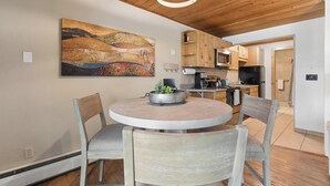 Eine moderne Küche mit Holzschränken, einem Esstisch mit Stühlen, einer Hängeleuchte und einem großen, abstrakten Gemälde an der Wand.