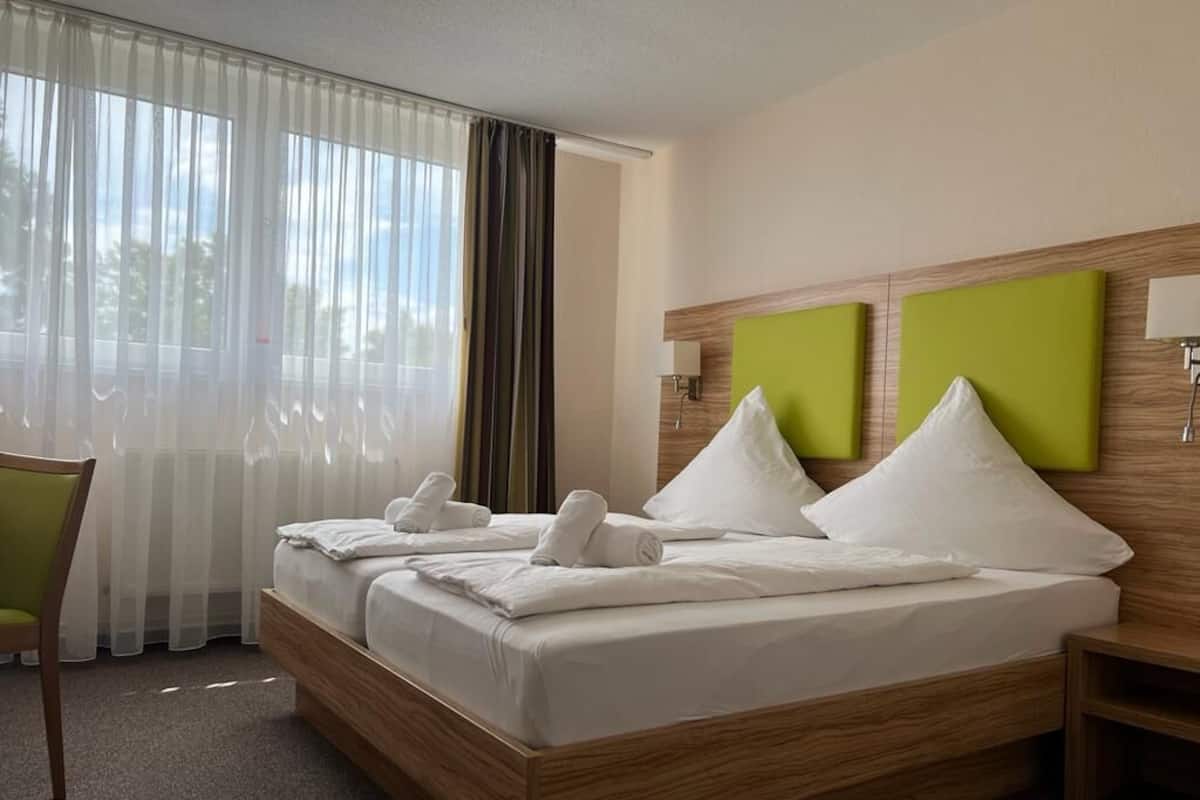 Een hotelkamer met een groot bed, een houten hoofdeinde, een groene accentmuur en een raam met dunne gordijnen.