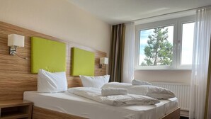 Ein Hotelzimmer mit einem hölzernen Bettgestell, zwei grünen Kopfteilen, weißer Bettwäsche, einem Nachttisch mit Lampe und einem Fenster mit Vorhängen.