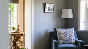 Una habitación con un sillón azul, una mesa redonda de madera, una lámpara y un cuadro en la pared.