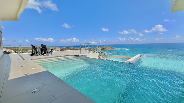 Ein Swimmingpool mit klarem, blauem Wasser, Blick auf den Ozean und einige Liegestühle.