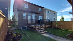 A two-story residential building with a wooden deck and a staircase leading to the second floor. - Delightful 1-Bedroom Private Suite in a New Home (Calgary)