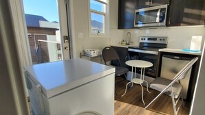 A compact kitchen with a microwave, oven, and sink. There is a small dining table and a chair. - Delightful 1-Bedroom Private Suite in a New Home (Calgary)
